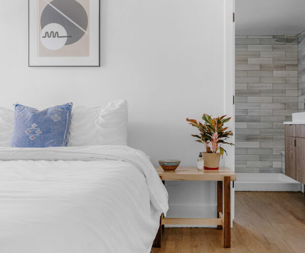 Bedroom with wood floor, bedside table with plant, plush bed, and door to bathroom.
